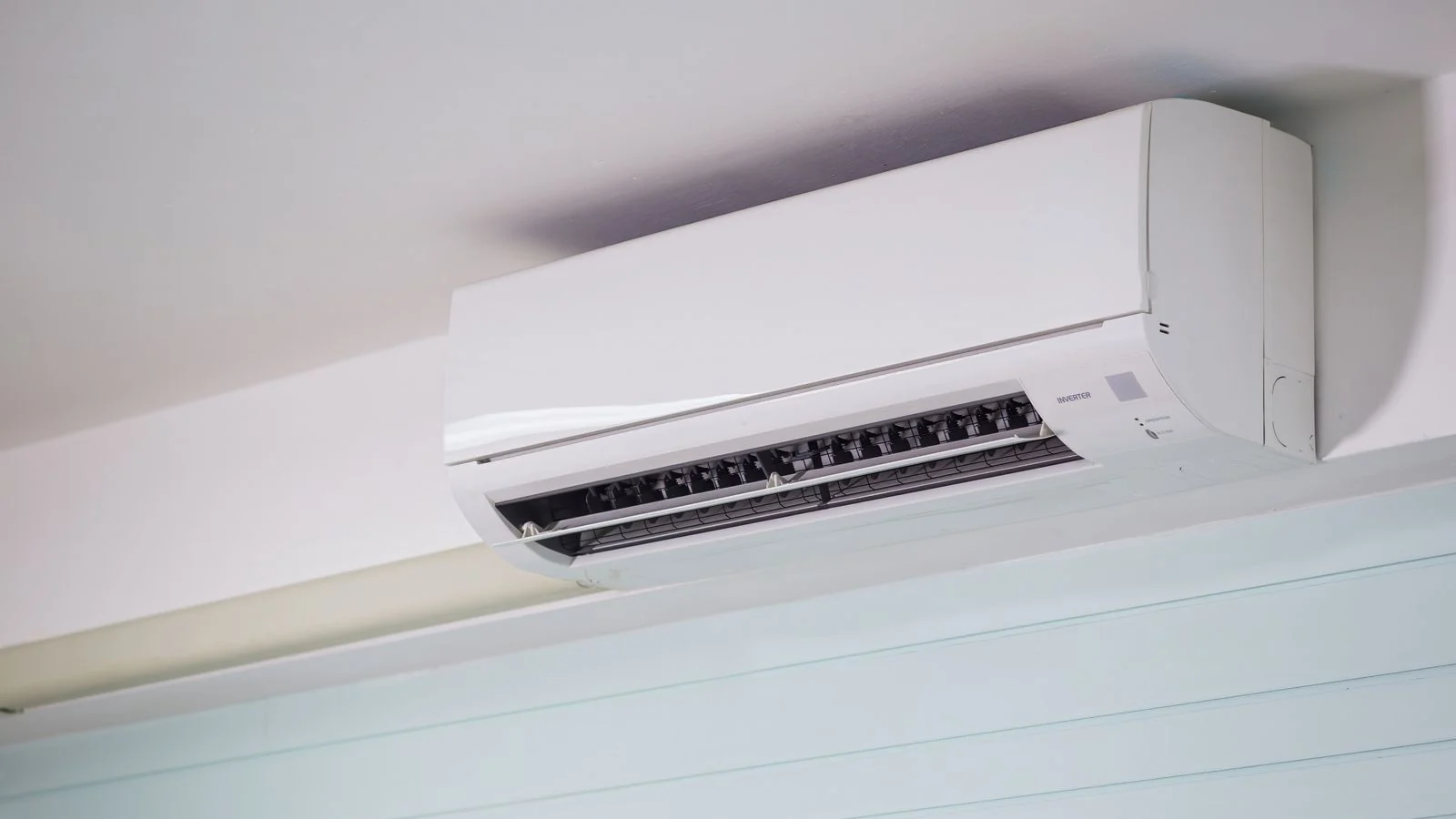 Unit aircond dinding jenis inverter berwarna putih dipasang tinggi di dinding bilik bercat biru muda dengan kipas terbuka, contoh unit yang diperiksa apabila aircond rumah tak sejuk.