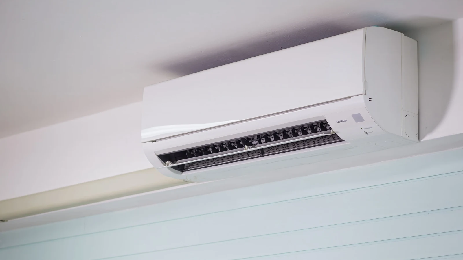 A wall-mounted indoor aircond with its louvres open, the blower barrel and coil visible through the outlet, the part a flushing aircond job actually cleans.