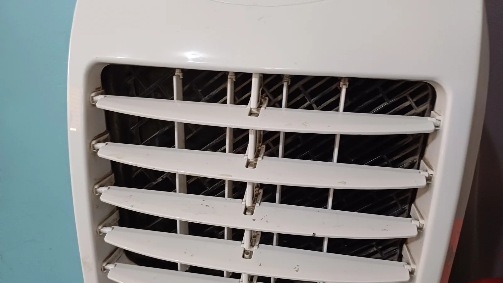 Close-up of the white louvred air outlet of a portable aircon not cold enough to cool its room, several slats slightly bent and scuffed.