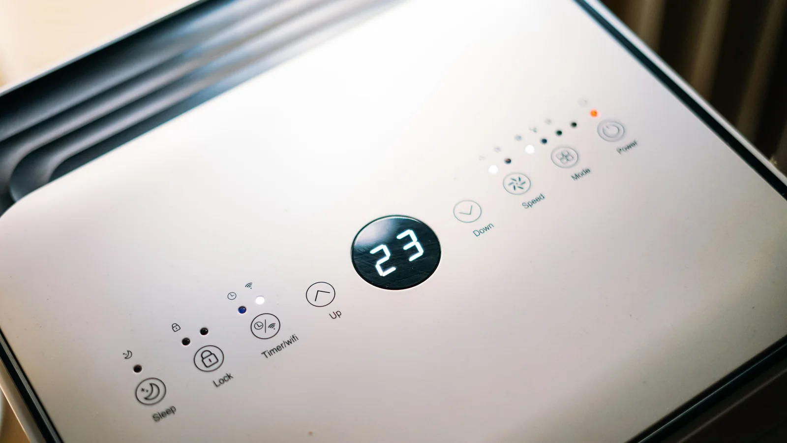 Close-up of a portable aircon control panel with a digital display reading 23 and touch buttons for sleep, timer, speed, mode and power.